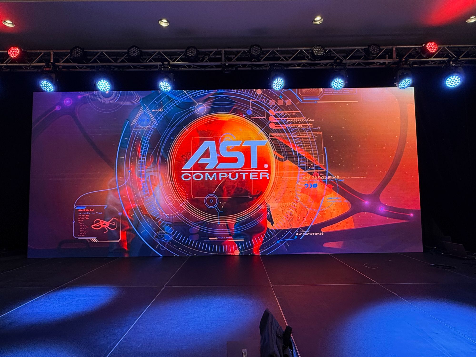 A single wide P2.6mm LED screen filling a corporate stage with a brand logo, lit from truss above