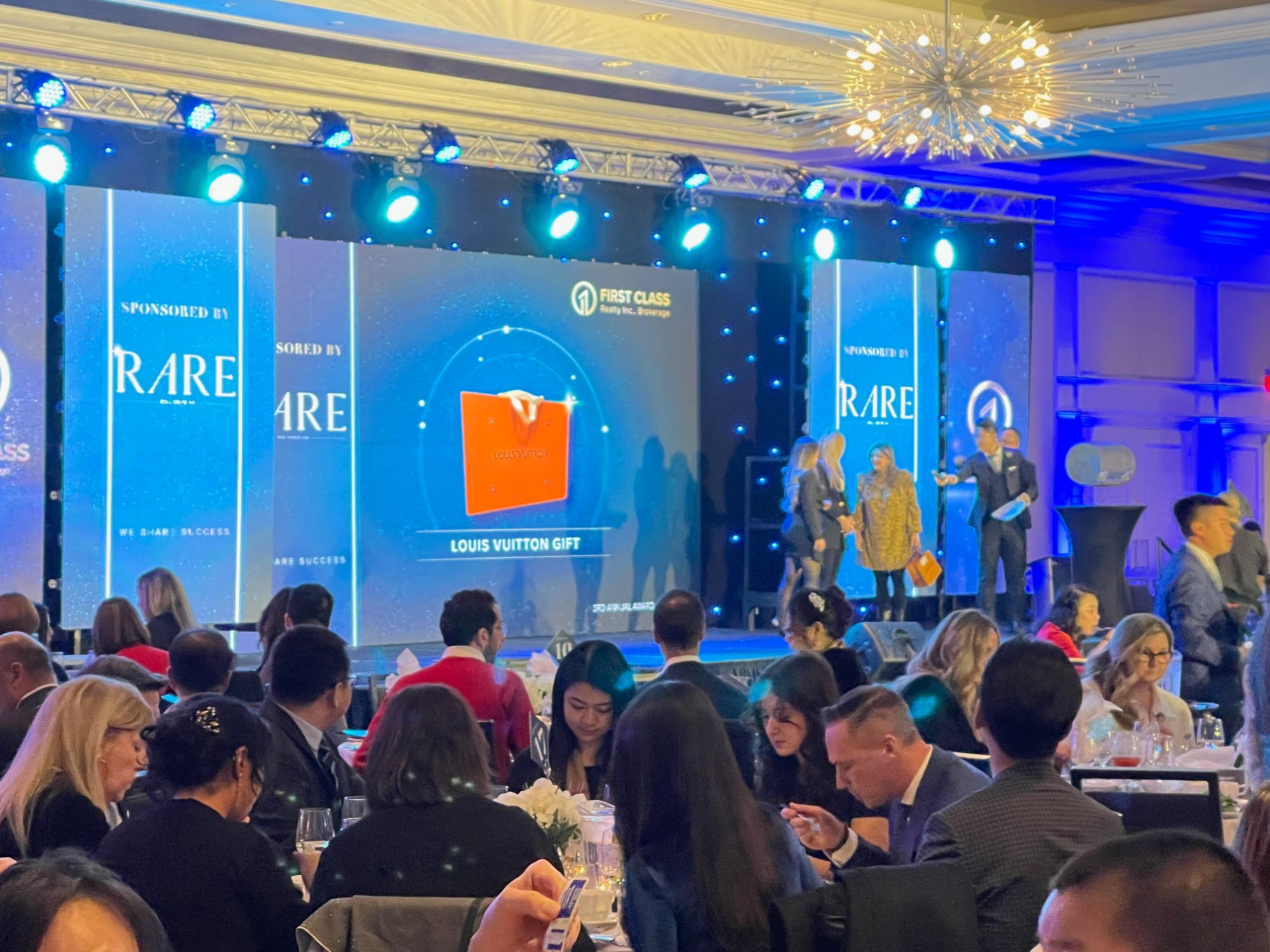 Corporate conference stage with a wide LED screen and two side screens in a hotel ballroom