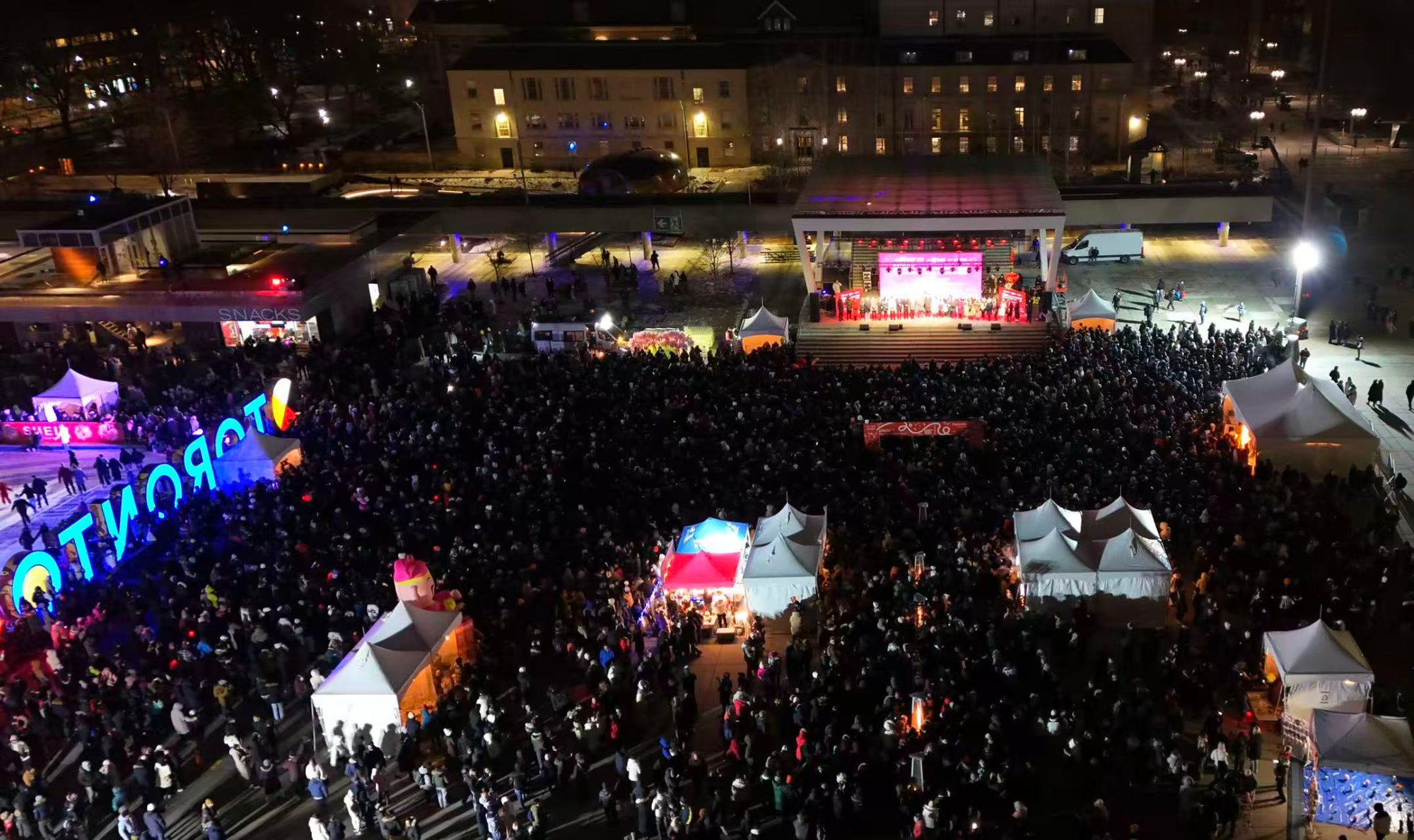 Aerial view of a large winter festival at Nathan Phillips Square — LED stage, tents and thousands of people