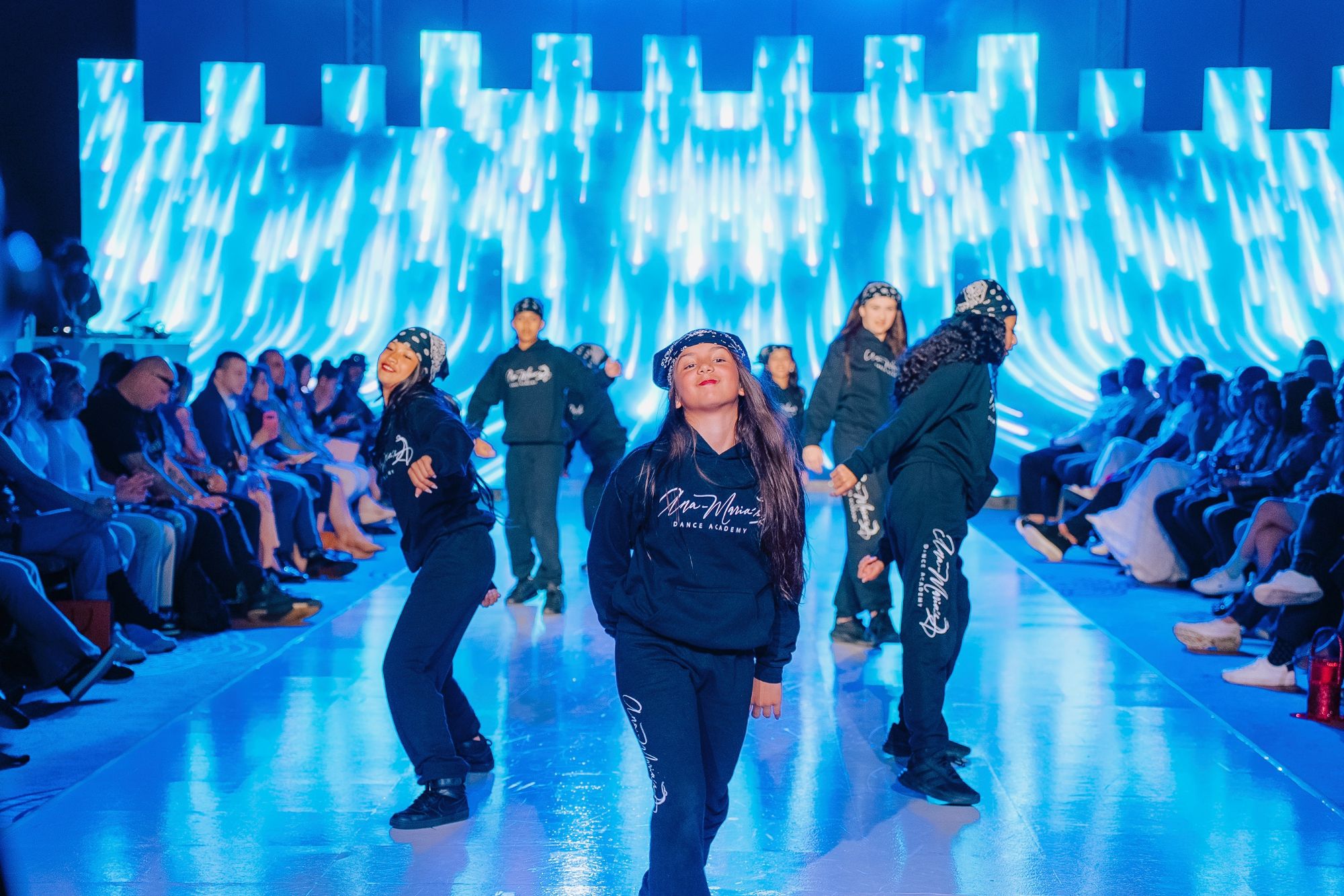 Dance crew performing on a runway with an LED wall behind them