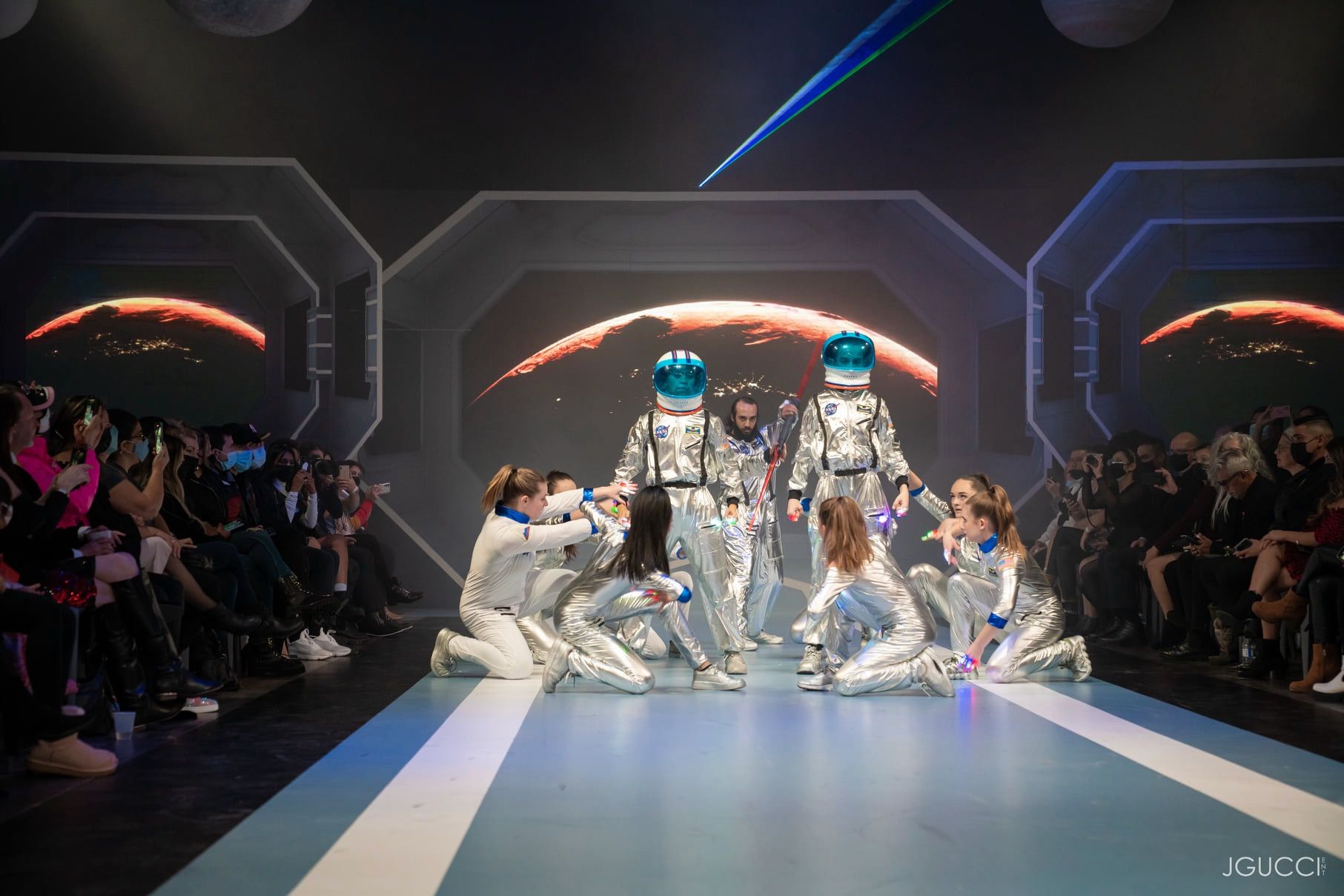 Astronaut-costumed performers kneeling on the runway in front of a Mars horizon on the LED wall