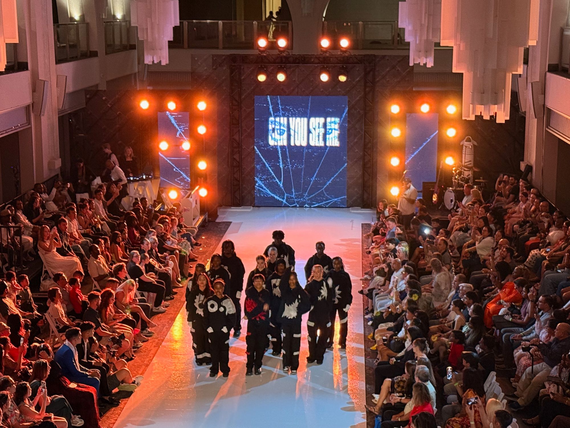Wide view of a runway show with LED backdrop, side towers and audience on both sides